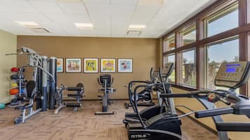 Un gimnasio con equipos de ejercicio variados, como cintas de correr y máquinas de pesas, y grandes ventanales que ofrecen luz natural.