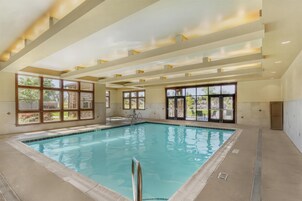Una piscina interior con paredes de vidrio transparente, suelo de baldosas e iluminación empotrada en el techo.