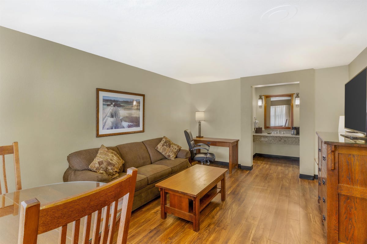 A living room with a wooden coffee table, a sofa, and a dining table. There is a kitchen area with a countertop and cabinets.