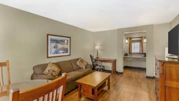 A living room with a wooden coffee table, a sofa, and a dining table. There is a kitchen area with a countertop and cabinets.