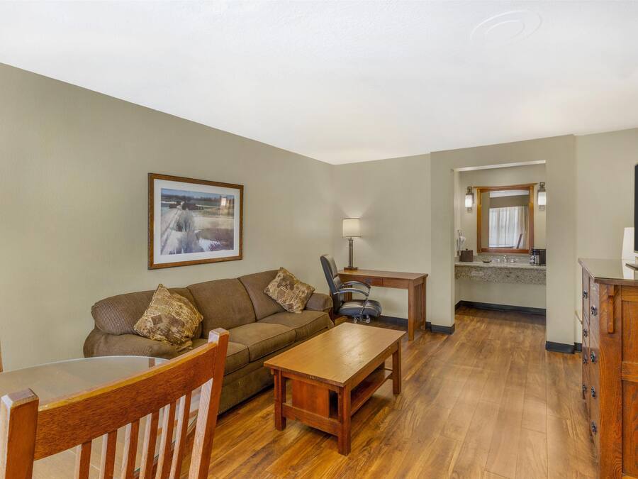 A living room with a wooden coffee table, a sofa, and a dining table. There is a kitchen area with a countertop and cabinets.
