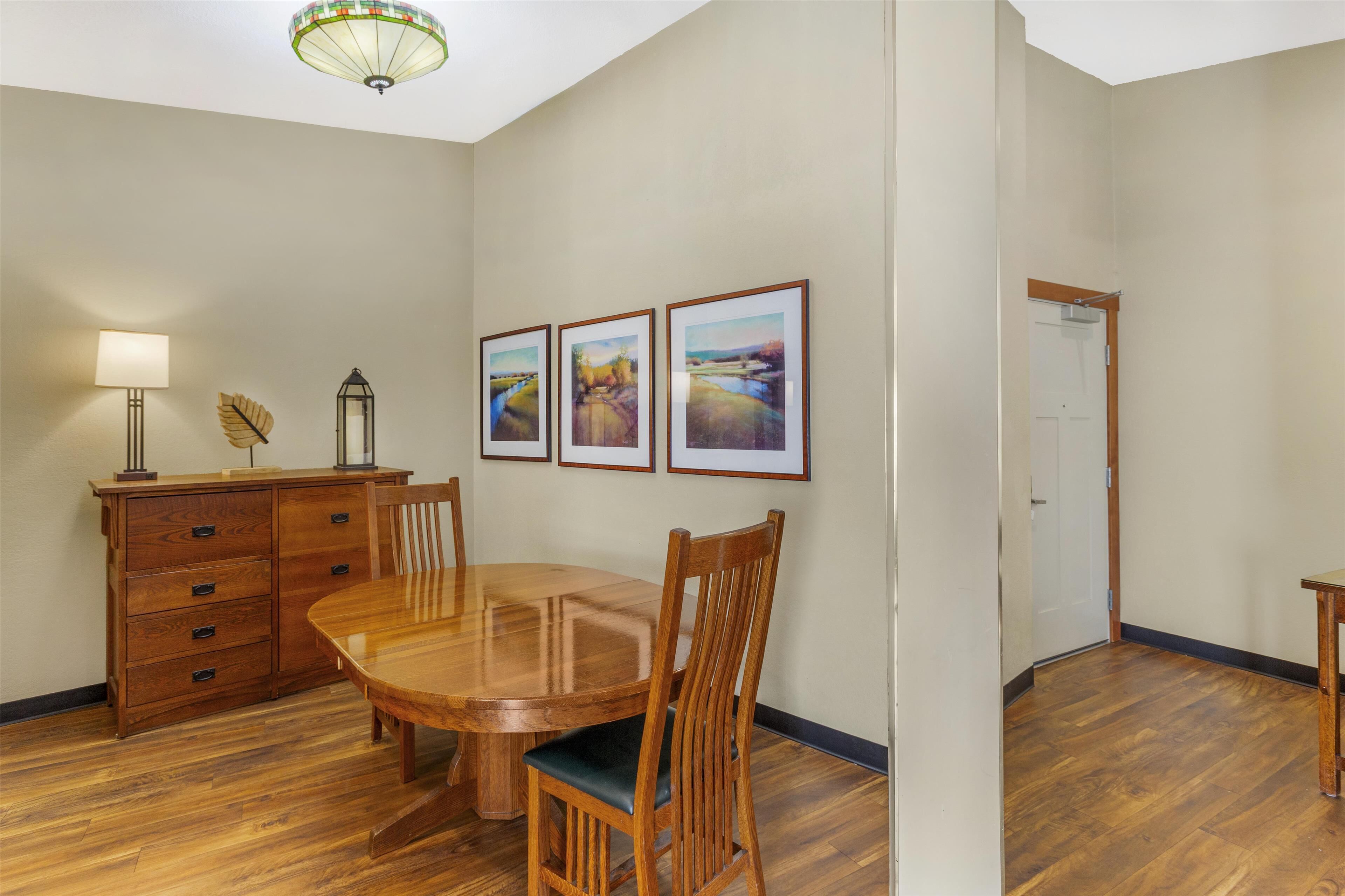 A dining area with a wooden table and chairs, a wooden cabinet with drawers, and three framed landscape paintings on the wall.