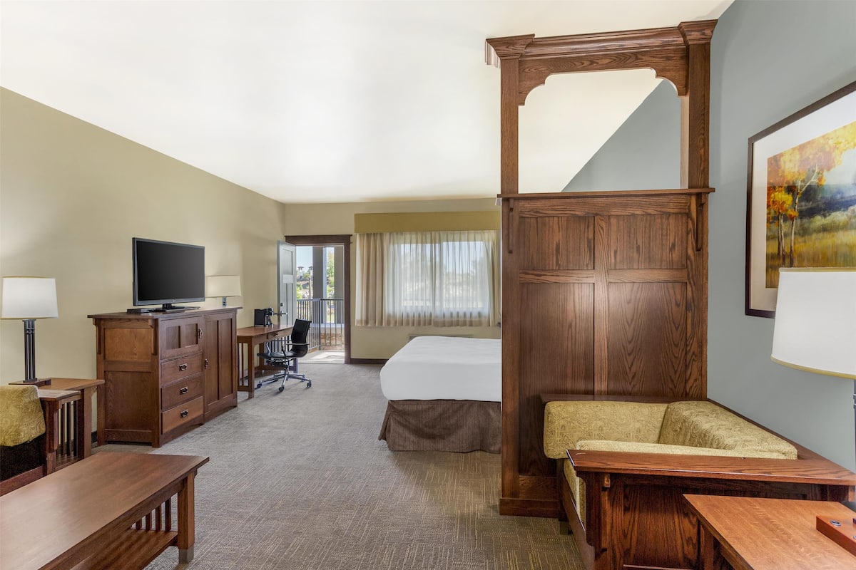 A hotel room with a large bed, wooden furniture, a desk, a television, and a painting on the wall.