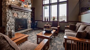 Relax in a comfortable seating area with a couch and chairs, surrounded by large windows offering a view of the outdoors and a stone fireplace.