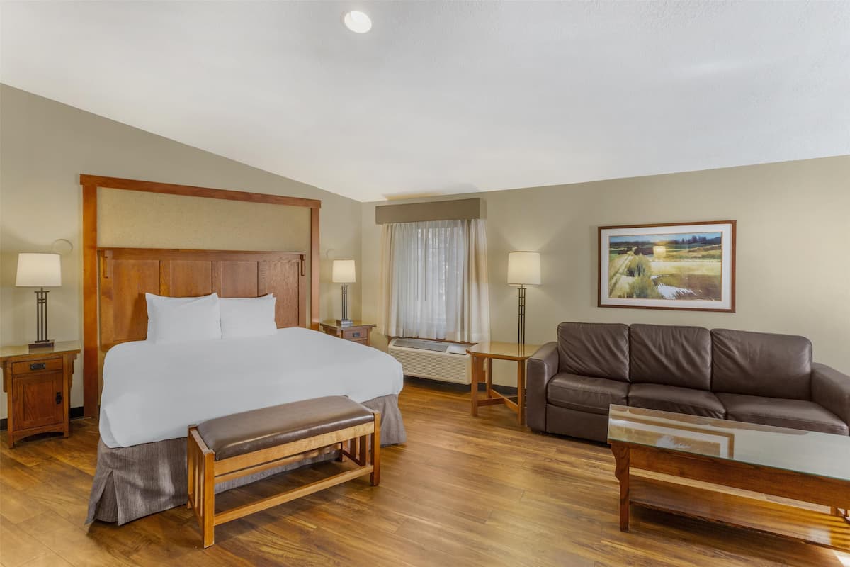 A hotel room with a large bed, a wooden bench, a sofa, and a painting on the wall.