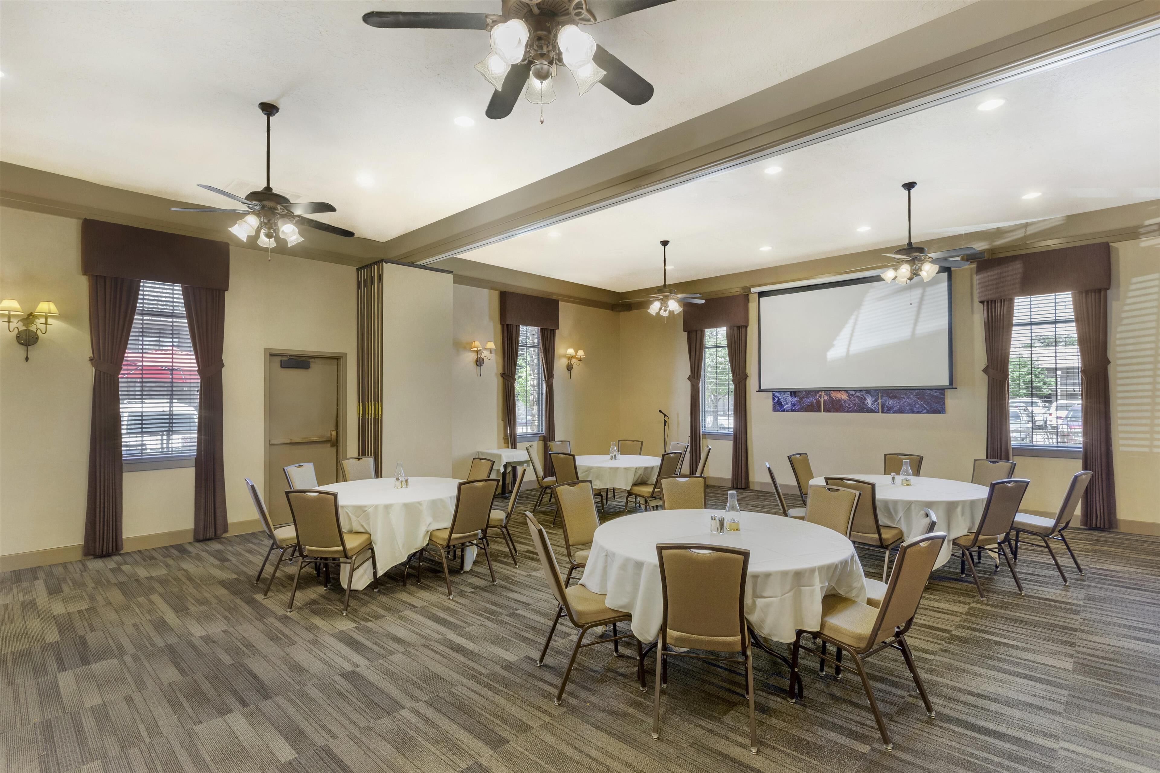 A conference room with round tables, chairs, ceiling fans, and wall-mounted lights.