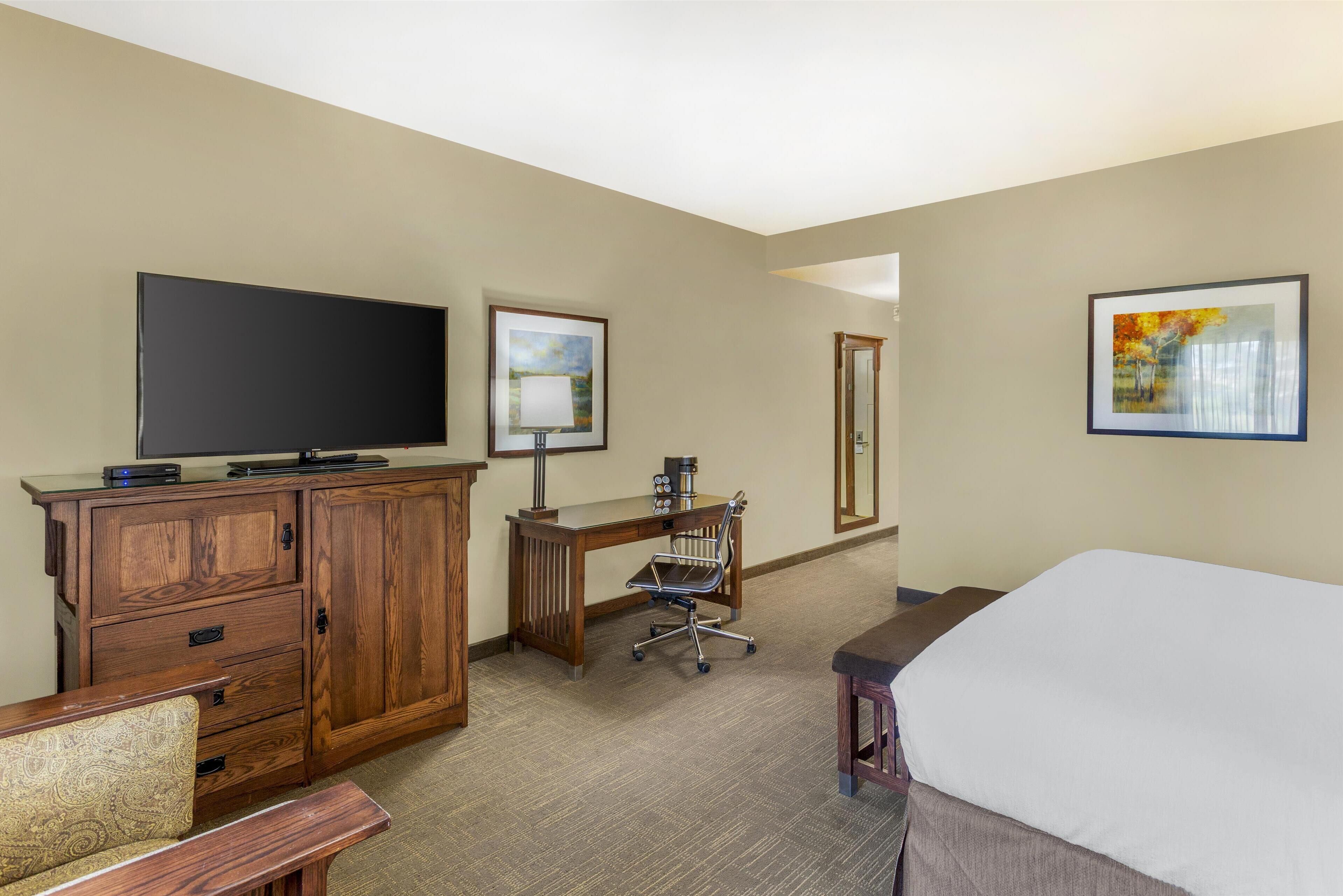 Ein Hotelzimmer mit Bett, Schreibtisch mit Stuhl, Fernseher und Bildern an den Wänden.
