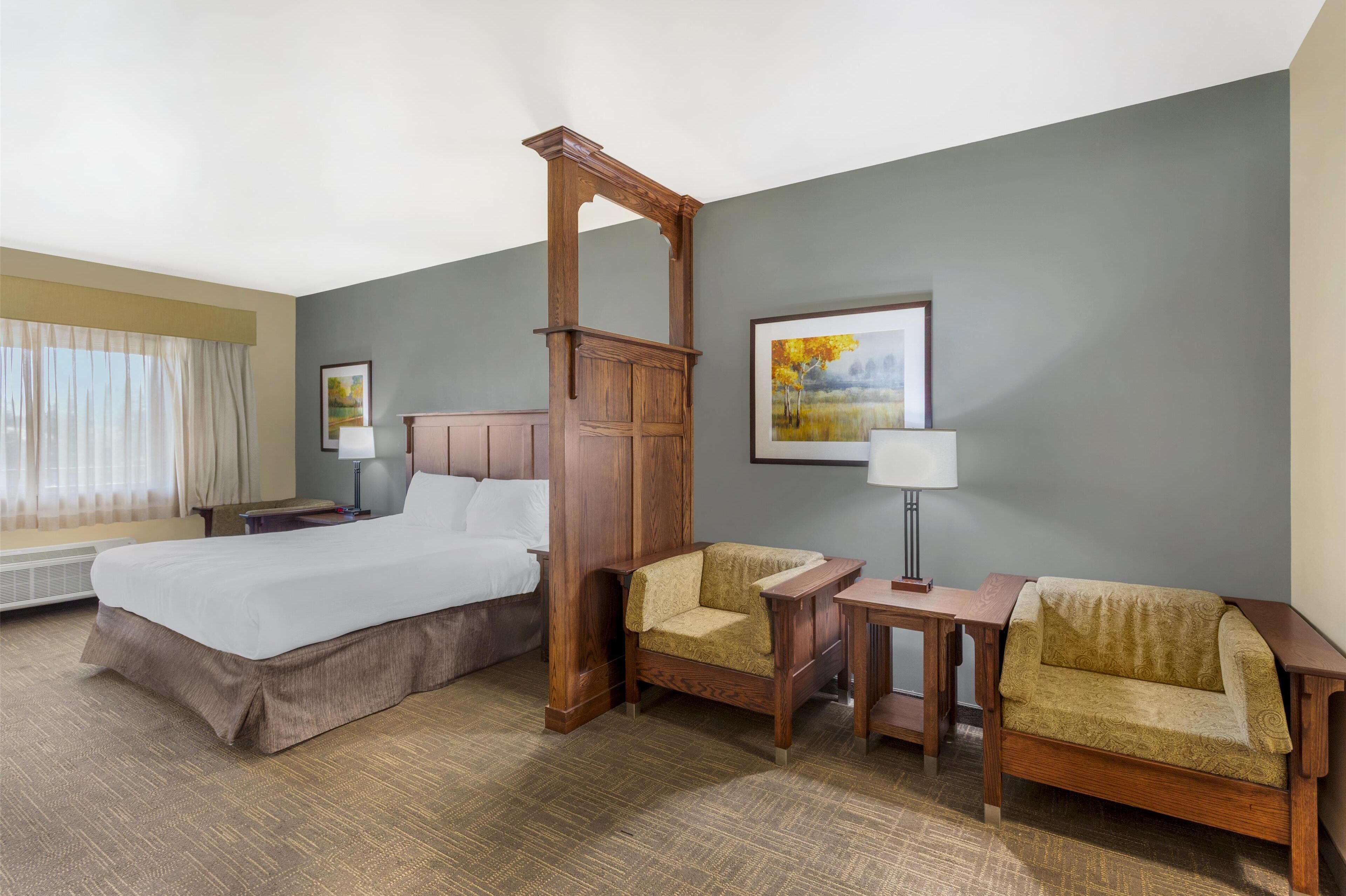 A hotel room with a large bed, two armchairs, a wooden nightstand, a table, and a painting on the wall.