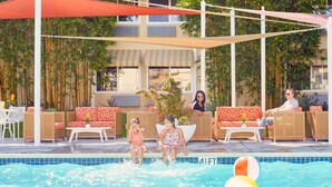 A poolside area with wicker furniture, umbrellas, and a view of a building with striped awnings.