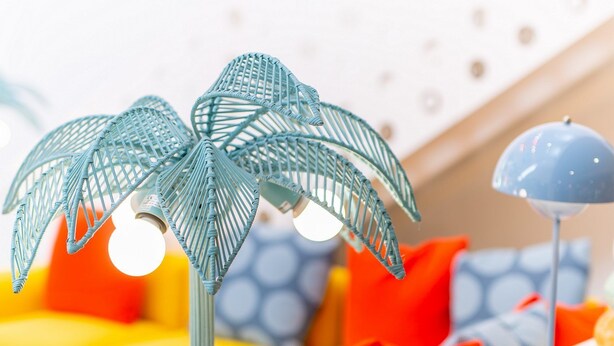 A room with a yellow sofa, a white bedside table, and a decorative palm tree lamp.