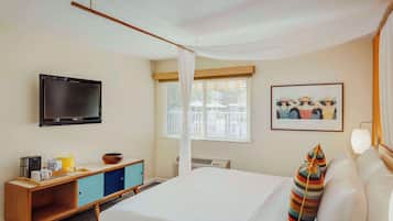 A hotel room with a bed, a TV, a window with blinds, a picture on the wall, and a bedside table with a lamp.
