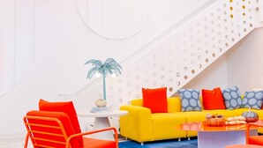 A modern interior with a staircase, a yellow sofa, red chairs, and a blue carpet.