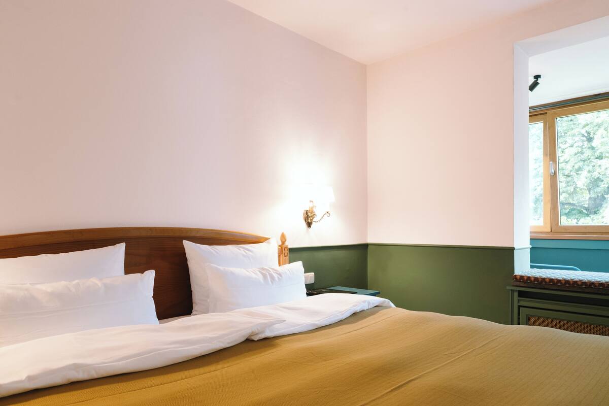Un lit bien fait, avec du linge de lit blanc, une tête de lit en bois et un mur d’accent vert.