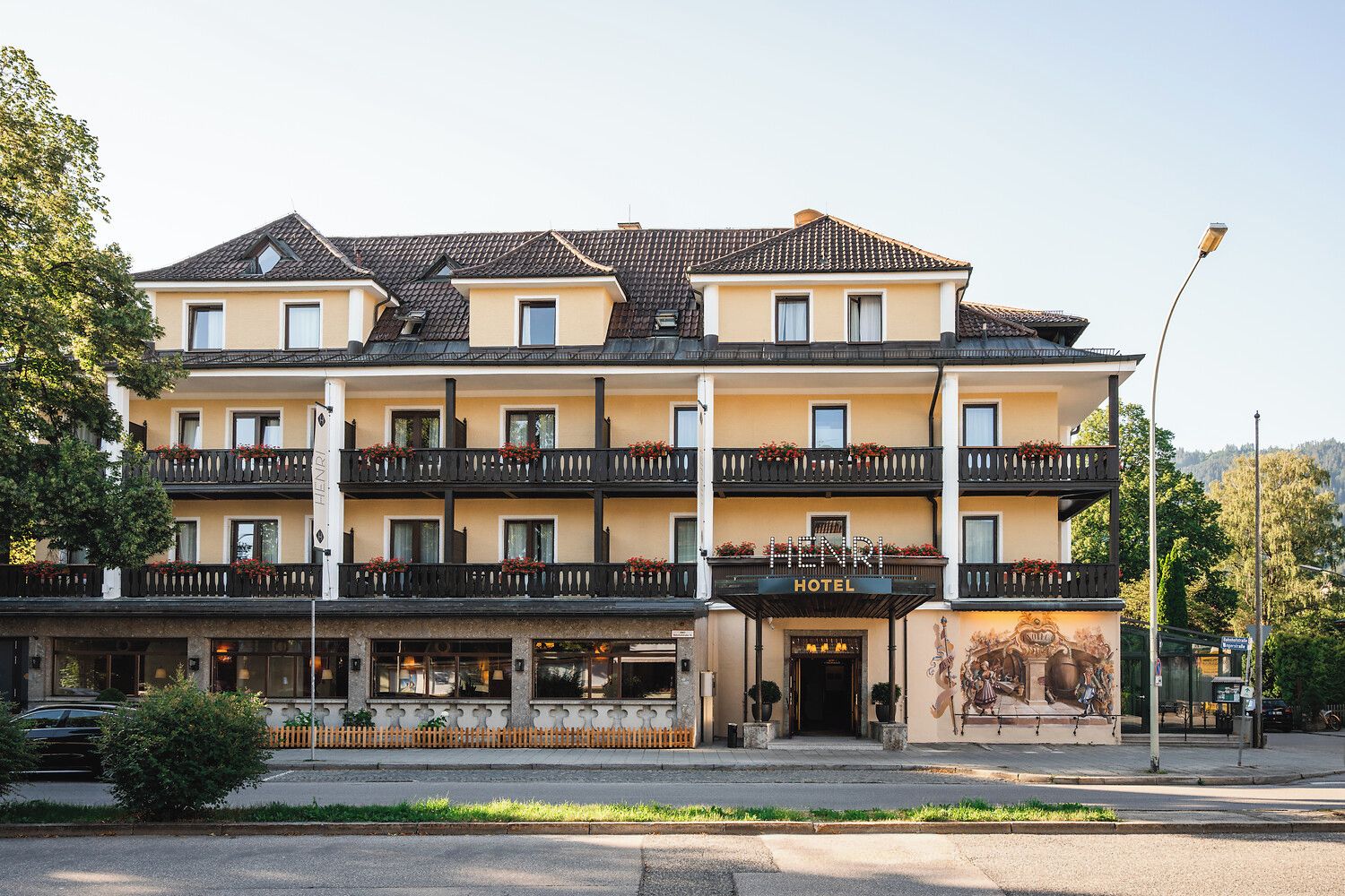 A multi-story hotel with a yellow facade, balconies with flower boxes, and a sign reading 'HENRI HOTEL'.
