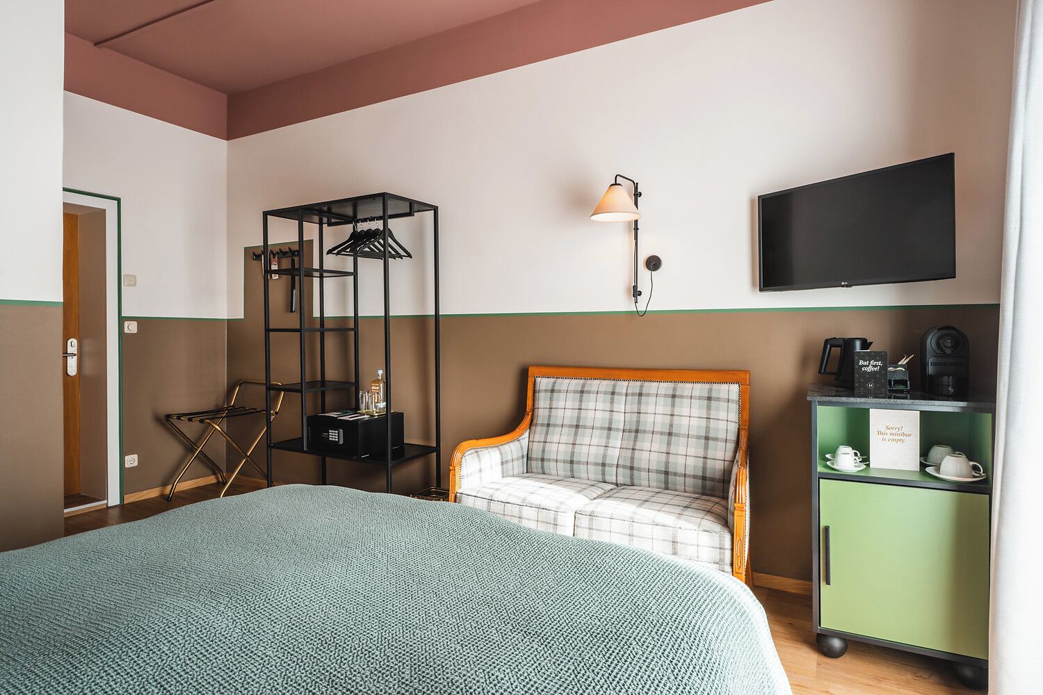 Una habitación de hotel con una cama, una silla, un televisor, un estante con una cafetera y un cartel.