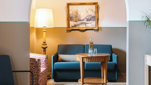 A cozy living room with a blue sofa, a wooden coffee table, and a lamp. - HENRI Hotel Garmisch-Partenkirchen (Neueröffnung) (Garmisch-Partenkirchen)