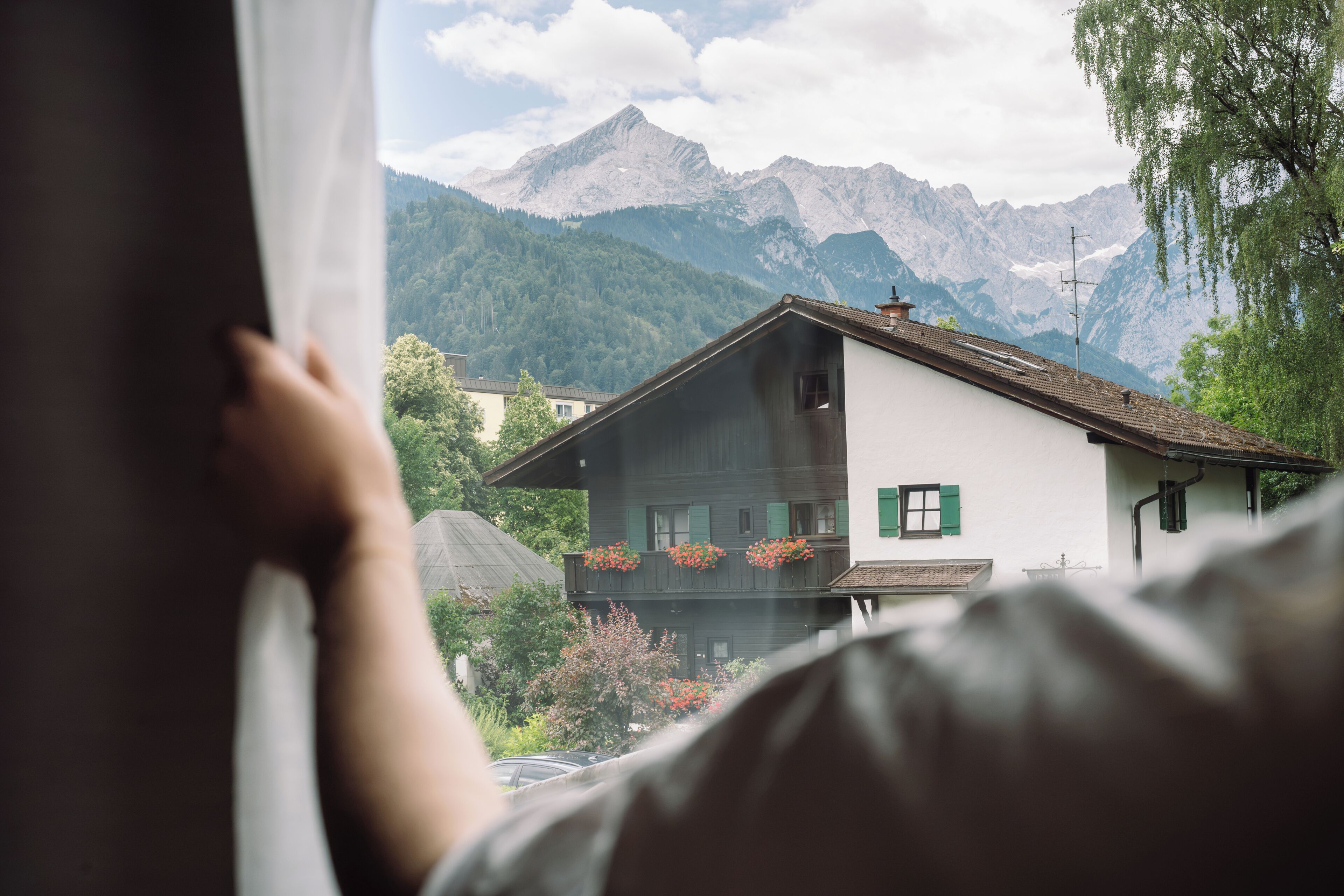 Blick auf eine Berglandschaft mit einem Haus und einer Person, die durch ein Fenster schaut.