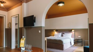 A hotel room with a bed, a TV mounted on the wall, a round wooden table with a bottle of champagne and glasses, and a small side table. - HENRI Hotel Garmisch-Partenkirchen (Neueröffnung) (Garmisch-Partenkirchen)