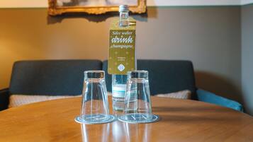 Una botella de agua y tres vasos sobre una mesa de madera en una habitación con un sofá y un cuadro en la pared.