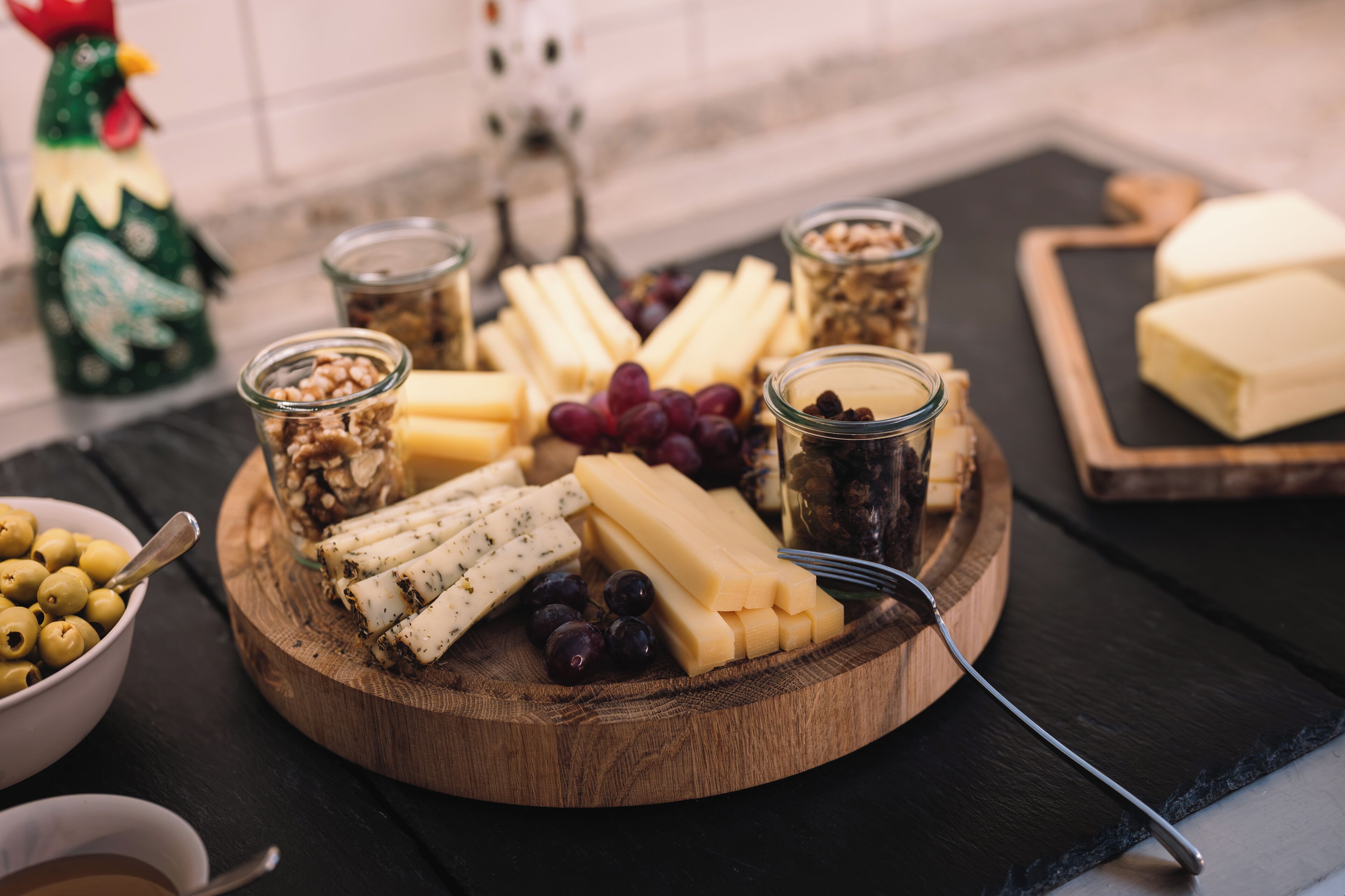 A wooden board with various cheeses, grapes, and nuts.