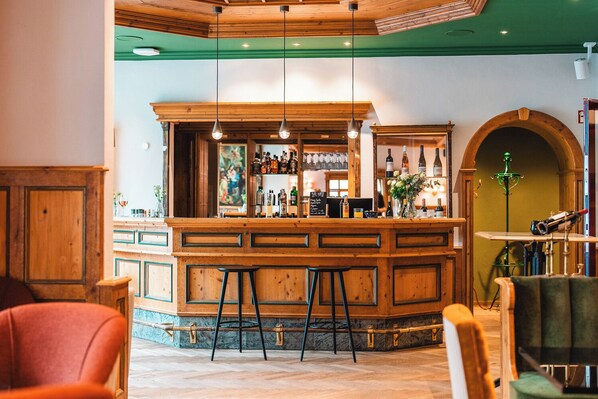 A bar area with wooden bar counter, stools, and a variety of bottles.