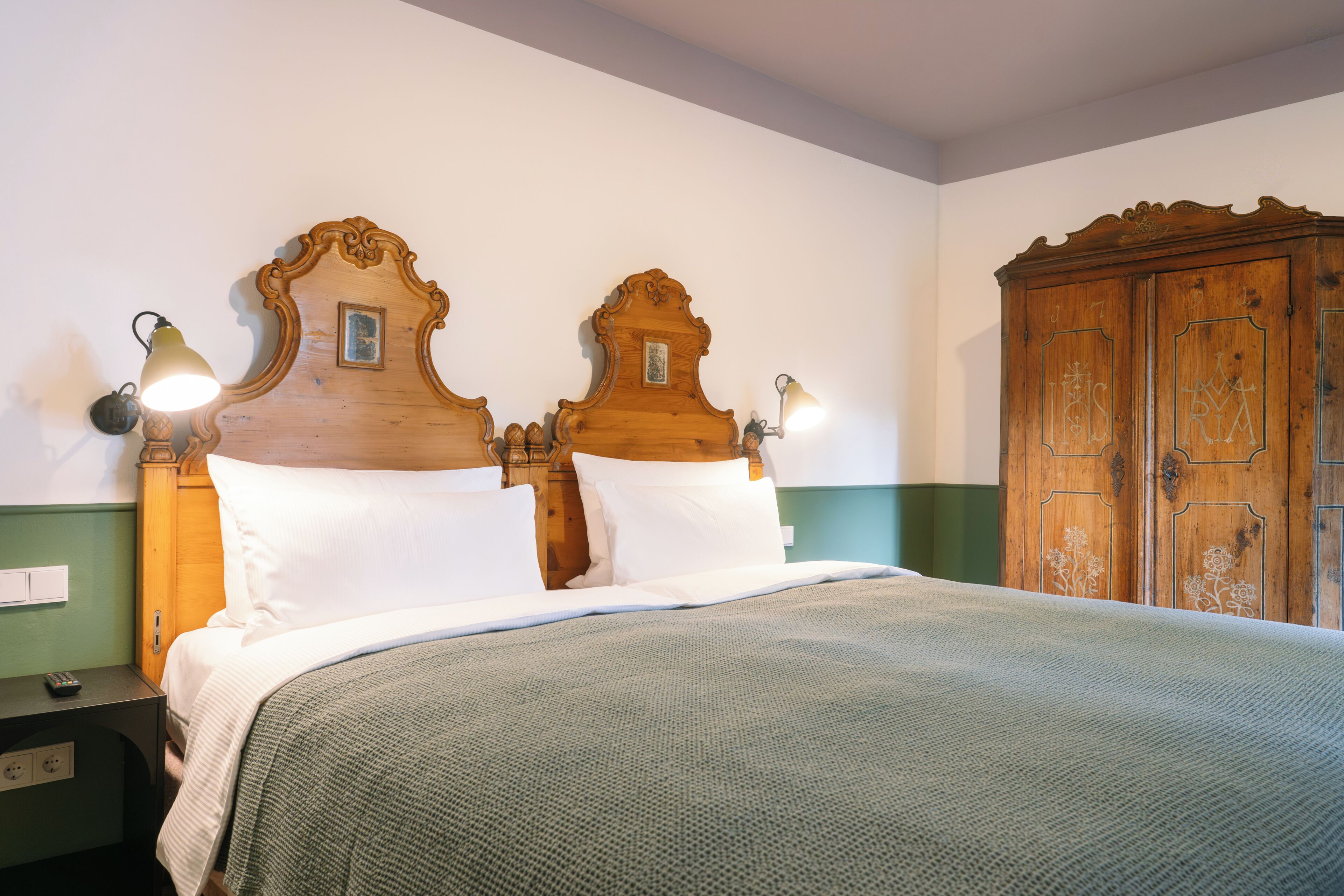 A double bed with a wooden headboard, two wall-mounted lamps, and a green wall.