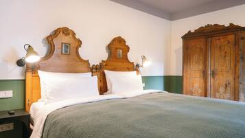 A double bed with a wooden headboard, two wall-mounted lamps, and a green wall.