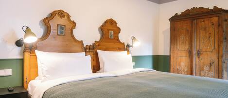 Een tweepersoonsbed met houten hoofdeinde, twee wandlampen en een groene muur.