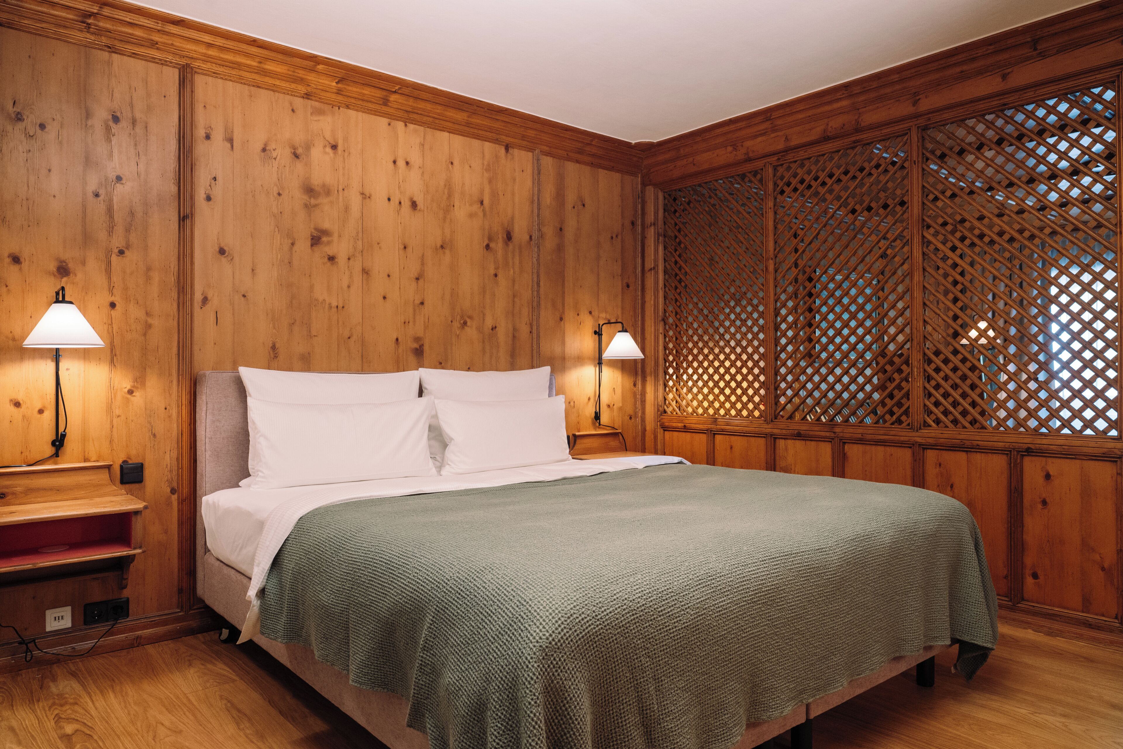 A wooden-paneled room with a bed, two bedside lamps, and a lattice partition.