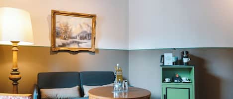 Ein gemütliches Zimmer mit einem blauen Sofa, einem Holztisch mit Gläsern, einer grünen Kommode mit Kaffeemaschinen und einem gerahmten Gemälde an der Wand.