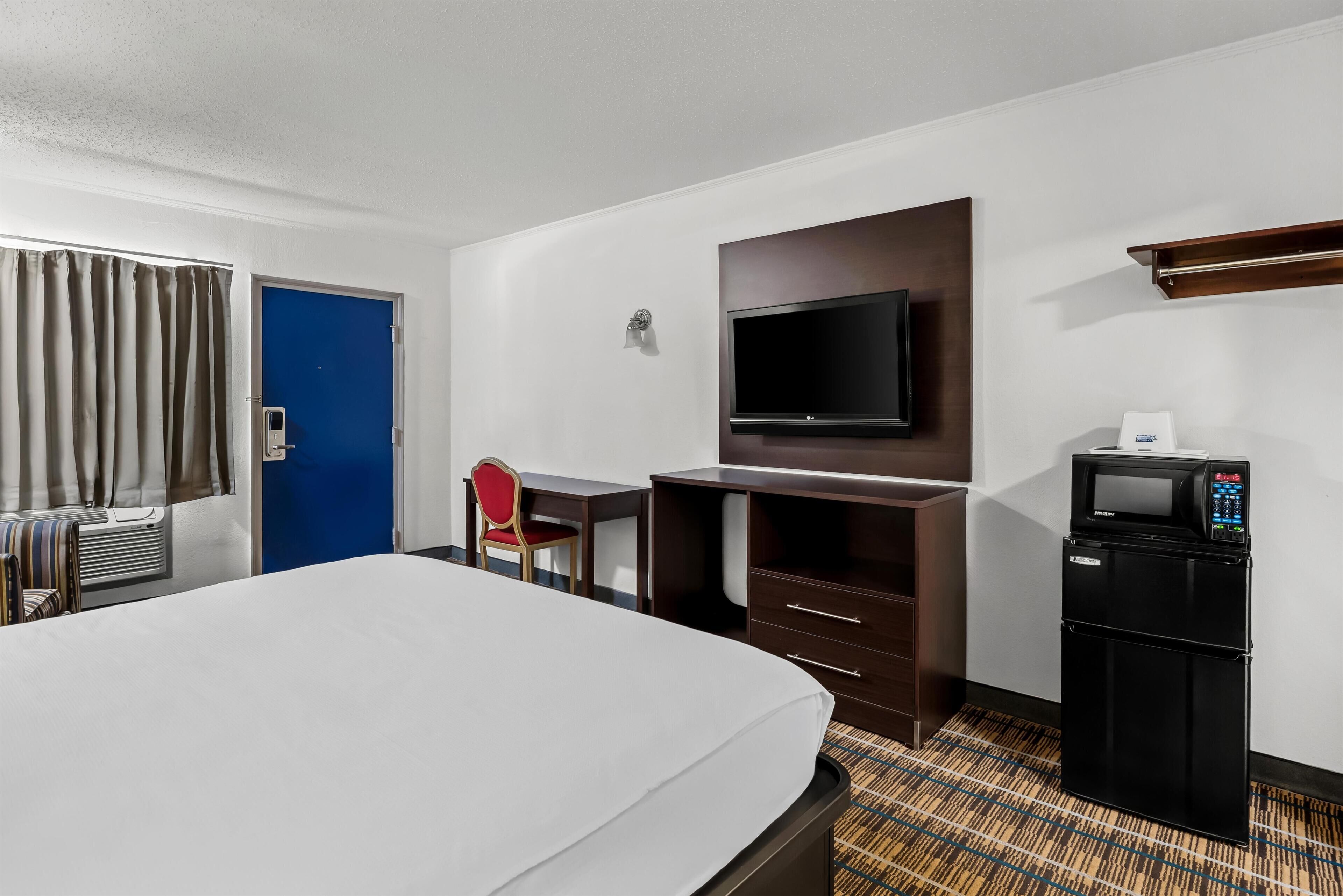 A hotel room with a bed, a desk, a chair, a television, a microwave, and a door.