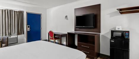 A hotel room with a bed, a desk, a chair, a television, a microwave, and a door.