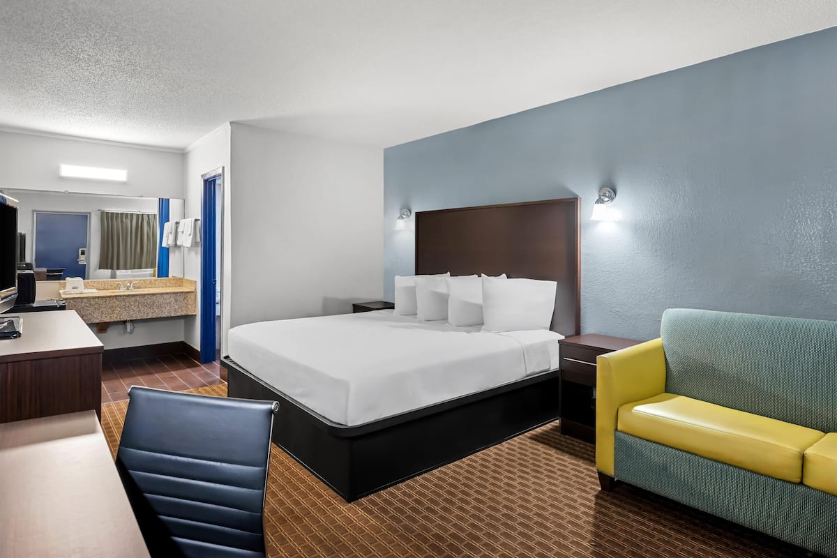 A hotel room with a bed, a desk, a chair, a sofa, a mirror, and a bathroom.