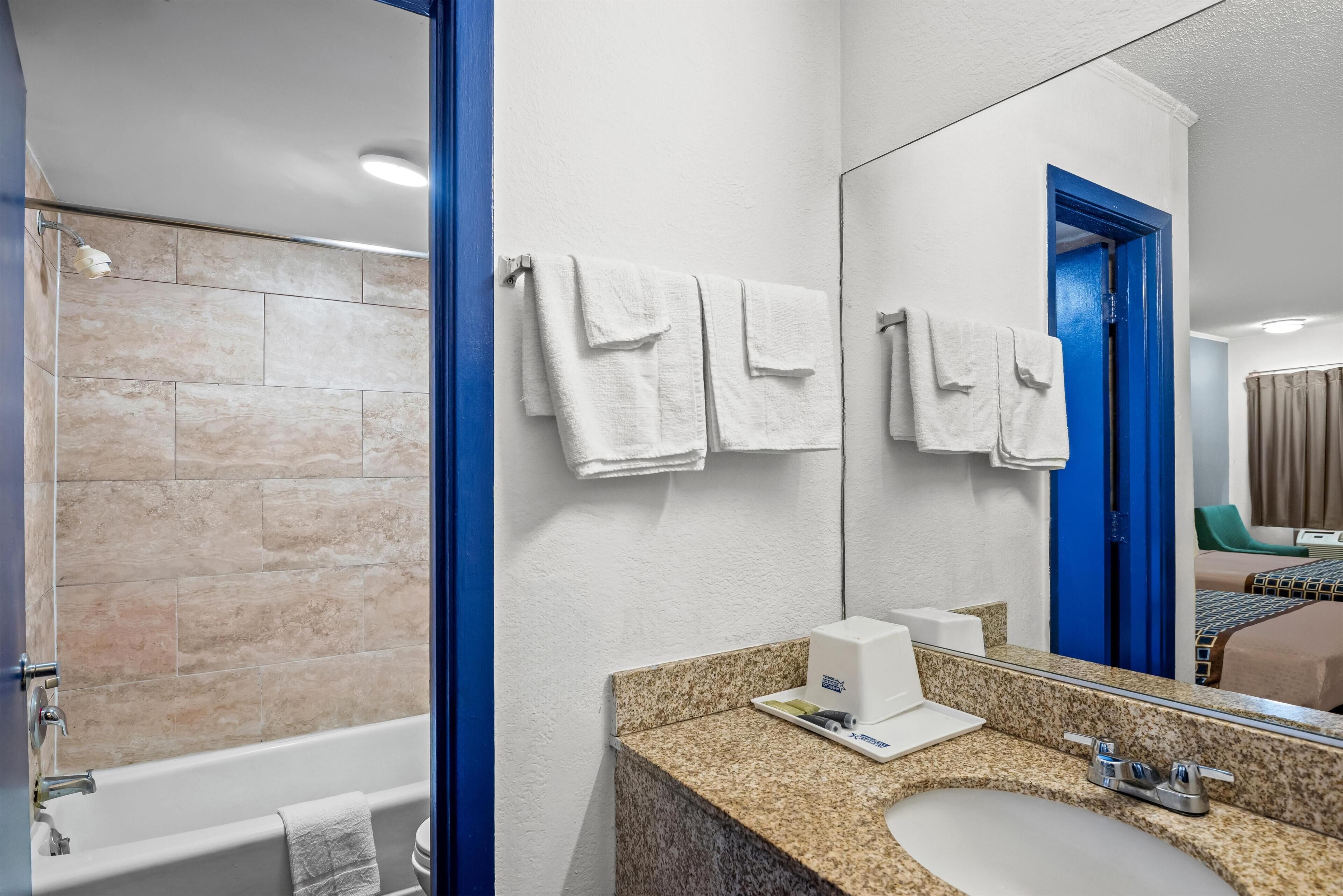 A hotel bathroom with a bathtub, a sink, a mirror, and towels on the wall.
