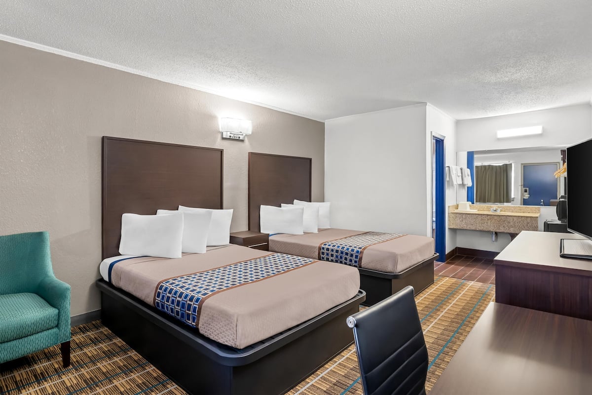 A hotel room with two beds, a desk, a chair, a mirror, and a bathroom.