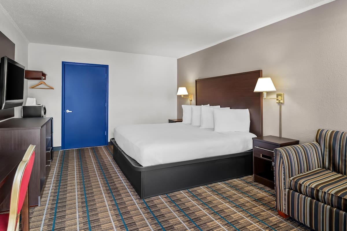 A hotel room with a bed, bedside tables, a TV, a desk, and a chair.