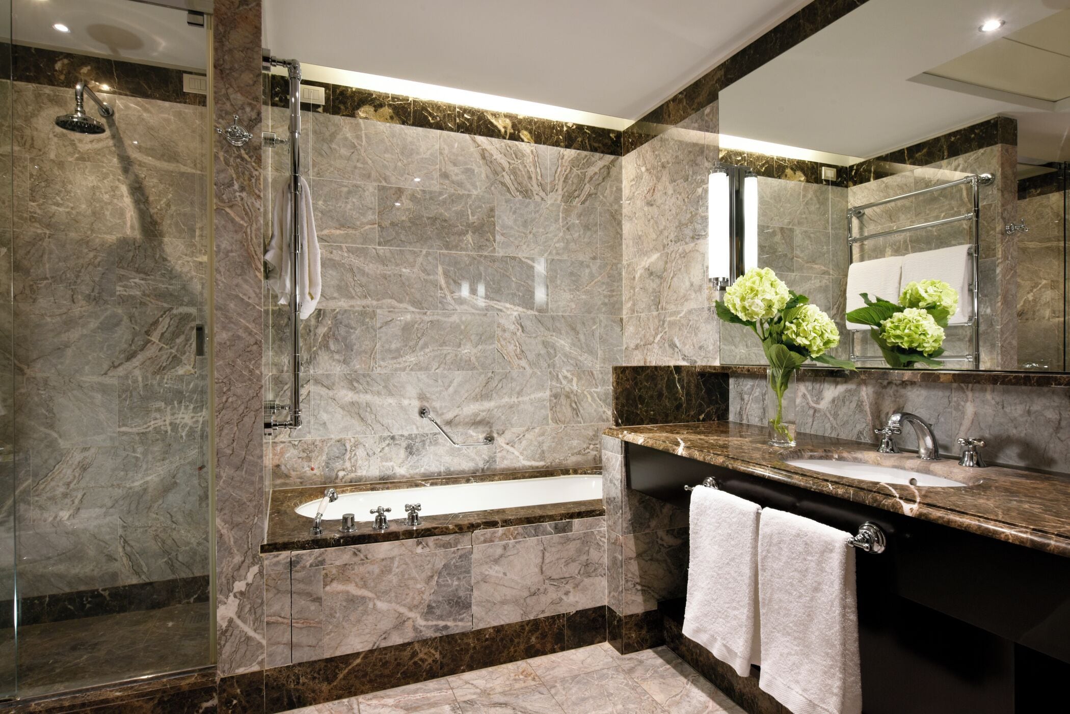 A modern bathroom with a glass-enclosed shower, a freestanding bathtub, and a marble-tiled vanity with a sink and mirror.