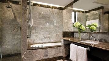A modern bathroom with a glass-enclosed shower, a freestanding bathtub, and a marble-tiled vanity with a sink and mirror.
