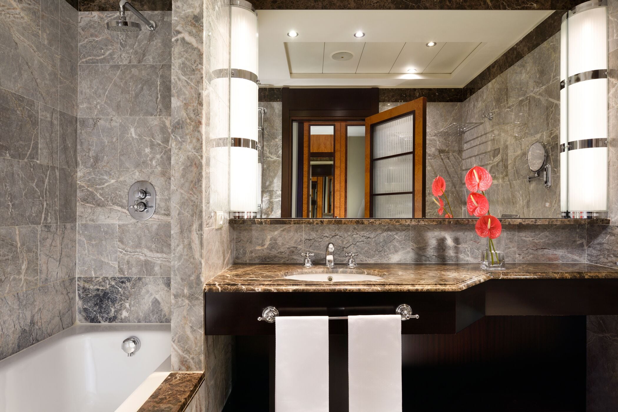 Un baño moderno con lavamanos de mármol, bañera y un espejo grande.