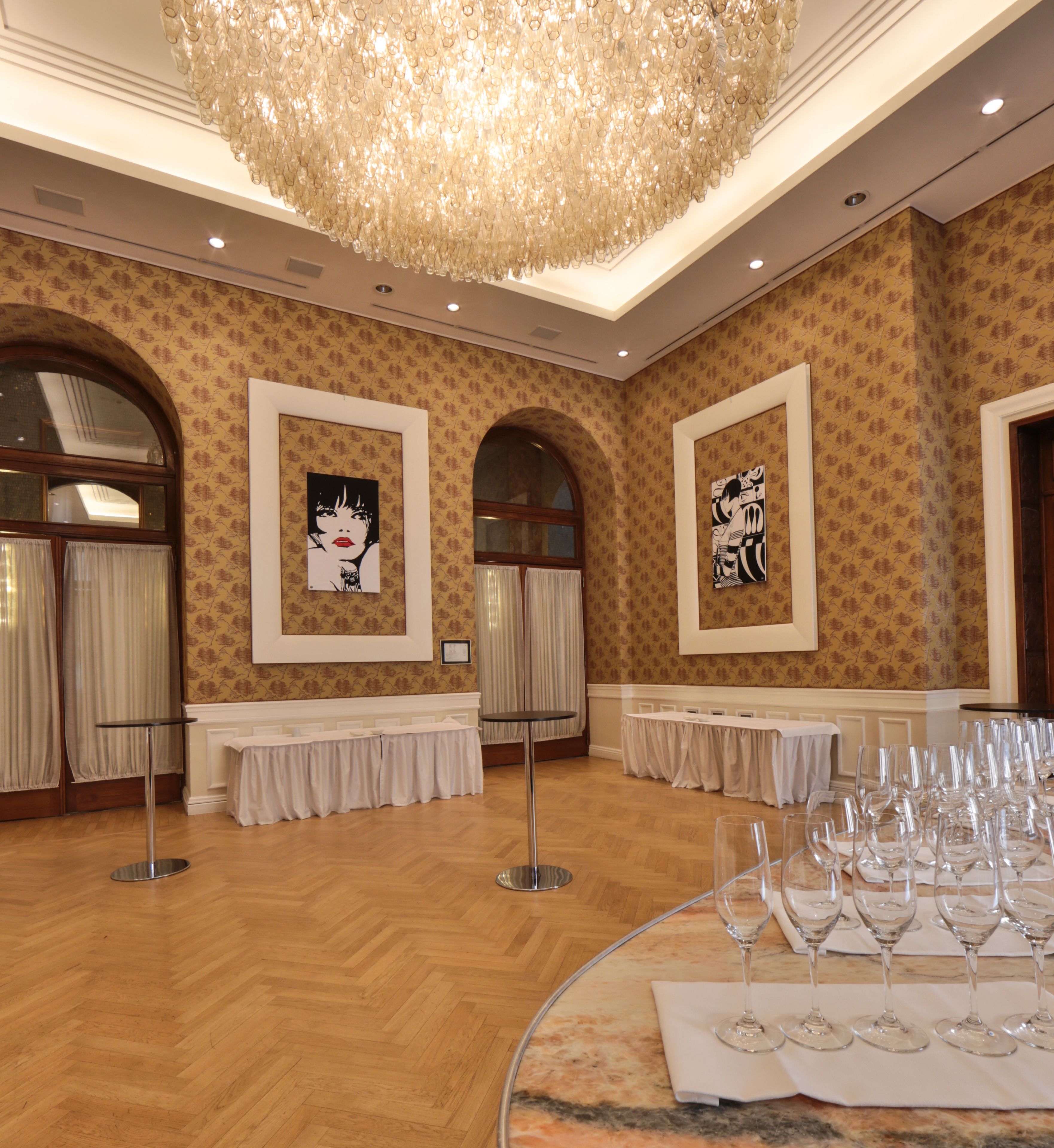 A banquet hall with wooden floors, chandeliers, framed artwork, and tables set for a formal event.