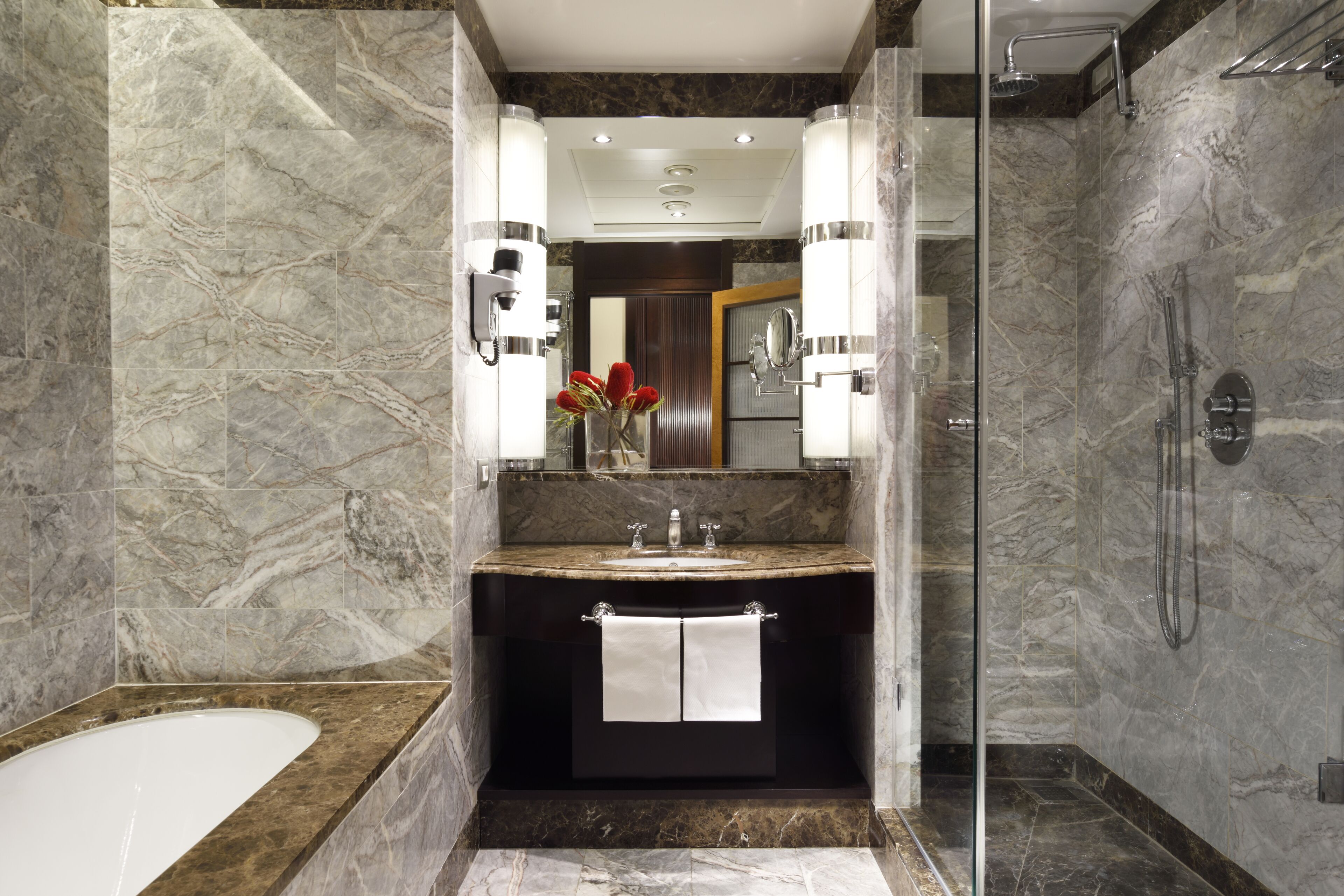 A modern bathroom with a marble vanity, a glass shower enclosure, and a visible bathtub.