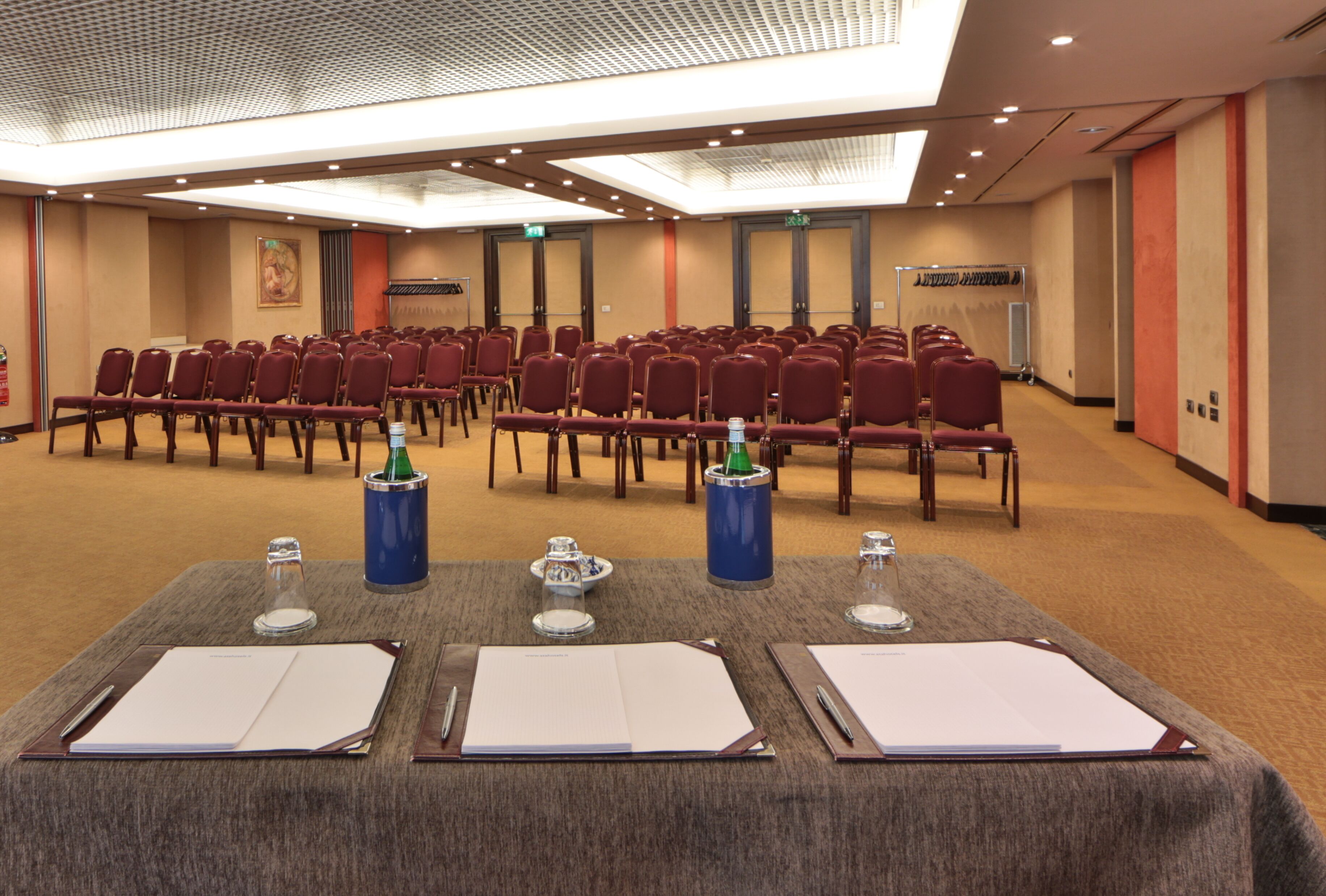 A conference room with rows of chairs, tables with notepads, and water bottles.