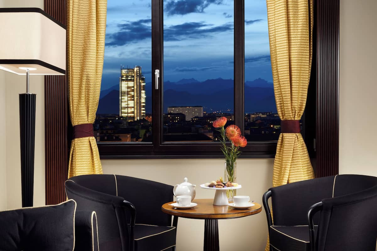 Ein Zimmer mit gedecktem Tisch für Tee, einer Blumenvase und Blick auf eine Stadtlandschaft mit Bergen.