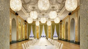 Una larga mesa de banquete con manteles blancos y sillas, rodeada de candelabros y cortinas decorativas.