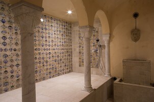 Une salle de bain avec des carreaux décorés, des colonnes en marbre et un espace douche.