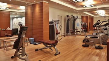 Una palestra con diverse macchine per esercizi, pavimento in legno e specchi alle pareti.