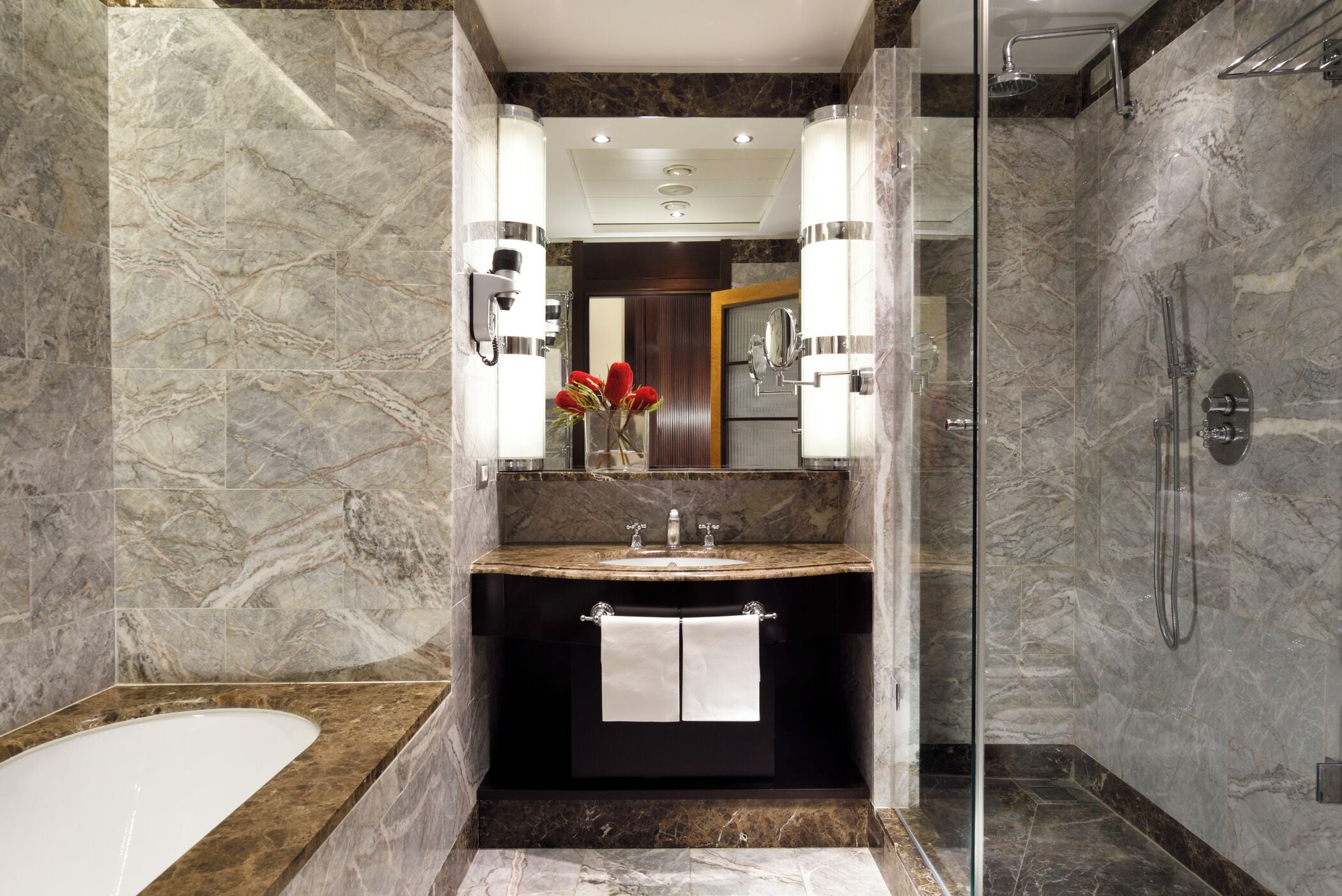 Un bagno moderno con lavabo in marmo, doccia vetrata e uno specchio grande.