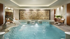 Una amplia piscina cubierta con pared de mosaico de piedra, sillas de descanso y una pequeña cascada.