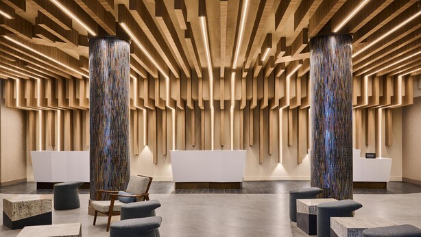 A modern reception area with a central desk, two large cylindrical columns, and several seating options. - Hilton Anchorage (Anchorage)