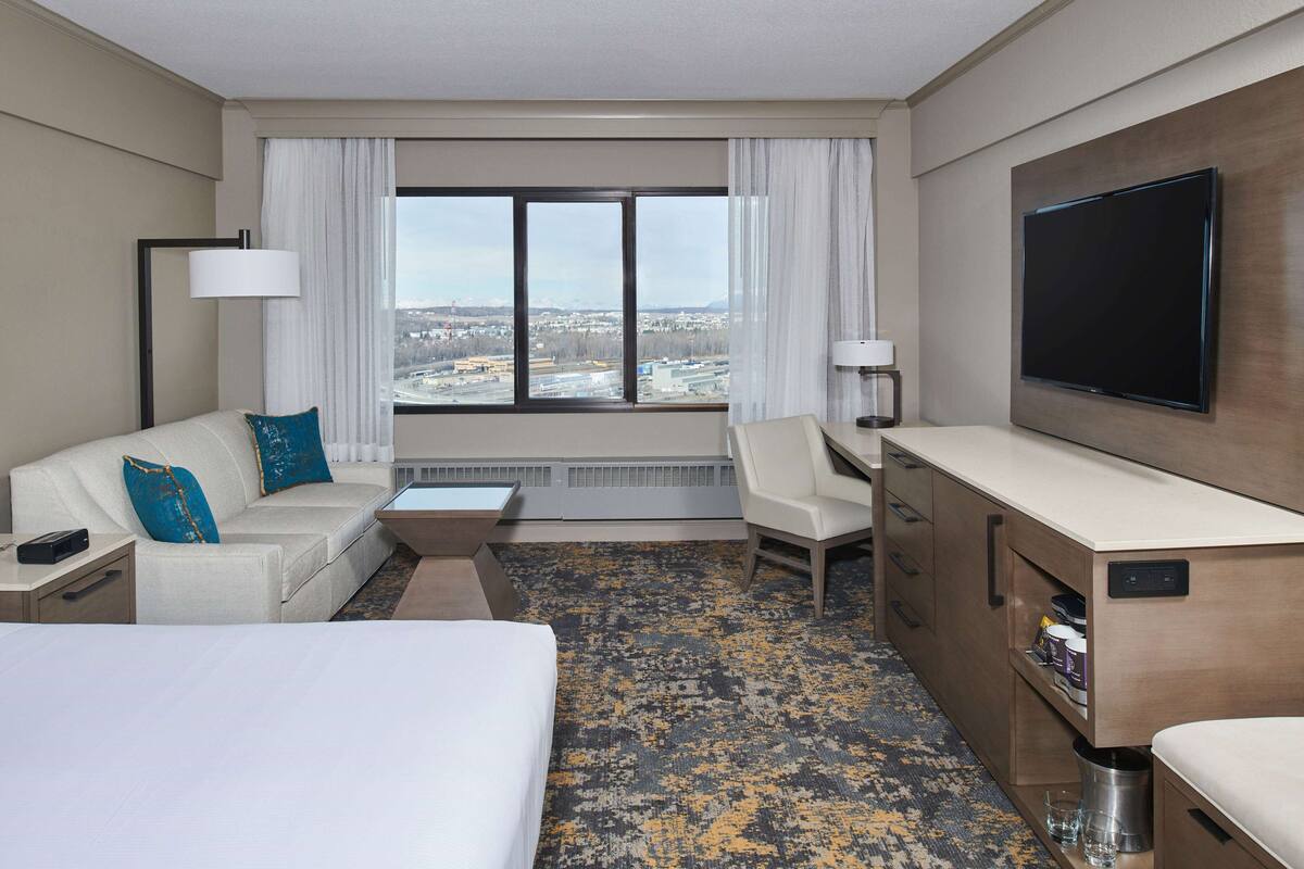 A hotel room with a bed, a sofa, a desk, and a TV.